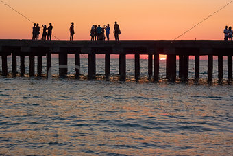 People on the old sea pier at sunset
