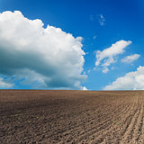black ploughed field under blue sky with clouds