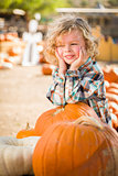 Little Boy Smiles While Leaning on Pumpkin at Pumpkin Patch