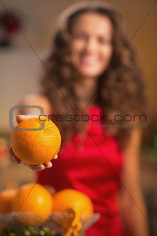 Closeup on orange in hand of young housewife in kitchen