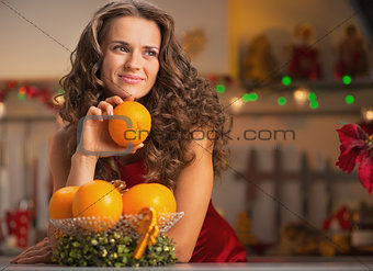 Thoughtful young housewife with orange in christmas decorated ki
