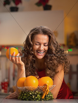 Happy young housewife with orange in christmas decorated kitchen