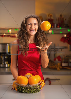 Smiling young woman throwing up orange in christmas decorated ki
