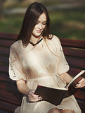 young woman sitting on bench reading book in autumn day