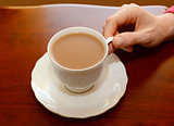 Woman picking up a cup of tea from a table