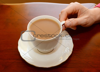 Woman picking up a cup of tea from a table
