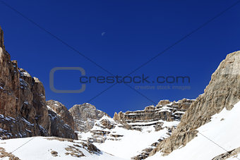 Snowy rocks and cloudless blue sky with moon