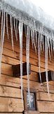 Wooden house with big icicles on snow-covered roof