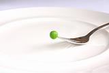 Single fresh green pea above white plate on fork.