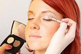 beautician is doing make-up to red-haired woman