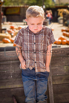 Frustrated Boy at Pumpkin Patch Farm Standing Against Wood Wagon