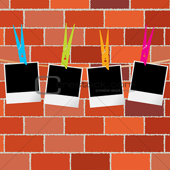 Blank photo frames with clothes pegs on rope over brick wall