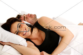 Woman laid smiling in white bed next to a sleeping man