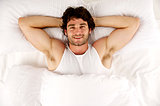 Man laid in white bed looking up at the camera smiling