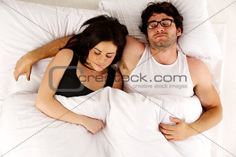 Man and woman laid in white bed asleep cuddling