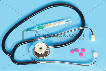 Phonendoscope, tablets and thermometer on a blue background