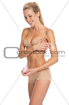 Smiling young woman in lingerie applying creme on arm