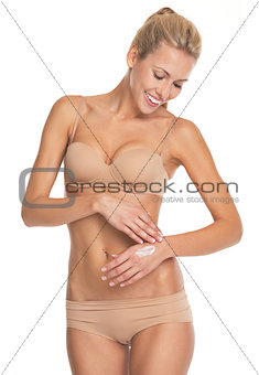 Smiling young woman in lingerie applying creme on hand