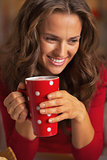 Happy young woman in christmas red dress having cup of hot bever
