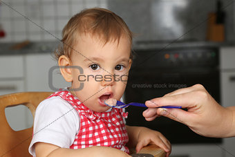Baby opening mouth, mother feeding it with porridge