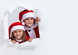 Happy kids in santa outfits looking through hole in paper