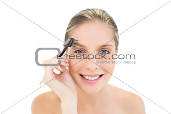 Happy fresh blonde woman brushing her eyebrows