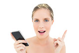 Surprised fresh blonde woman holding a mobile phone and pointing her finger