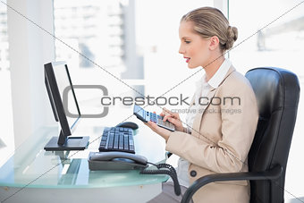 Side view of cheerful blonde businesswoman using calculator