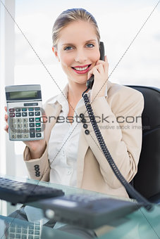 Smiling blonde businesswoman on the phone showing calculator