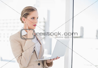 Pensive blonde businesswoman using laptop
