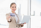Cheerful blonde businesswoman showing credit card holding laptop