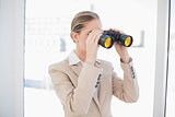 Serious blonde businesswoman looking through binoculars