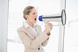 Angry blonde businesswoman shouting in megaphone