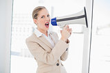 Furious blonde businesswoman shouting in megaphone