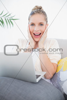 Excited fresh model using laptop sitting on sofa
