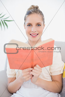 Smiling fresh model reading book sitting on sofa