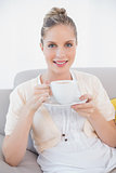 Smiling fresh model holding coffee sitting on sofa