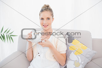 Happy fresh model holding coffee sitting on sofa