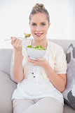 Happy fresh model holding healthy salad sitting on sofa