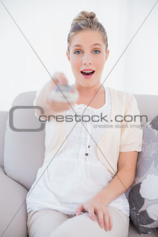 Surprised fresh model changing tv channel sitting on sofa