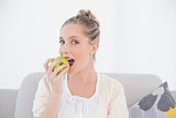 Gorgeous model eating green apple sitting on sofa
