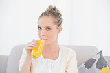 Gorgeous model drinking orange juice sitting on sofa