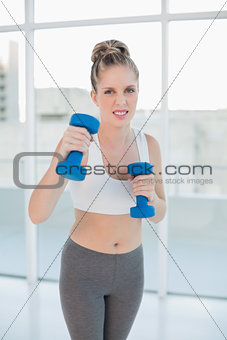 Competitive sporty blonde exercising with dumbbells