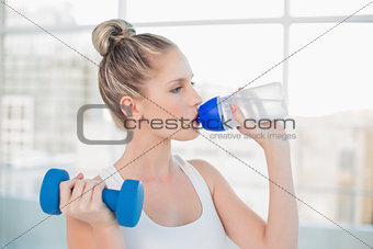 Peaceful sporty blonde drinking water while lifting dumbbell