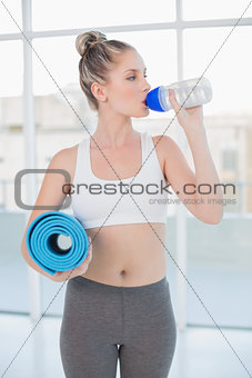 Sporty blonde drinking water holding exercise mat