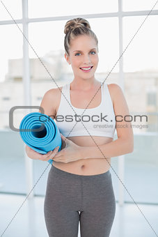 Smiling sporty blonde holding balled up exercise mat