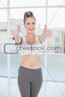 Smiling sporty blonde listening to music giving thumbs up