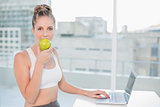 Sporty blonde eating apple while using laptop
