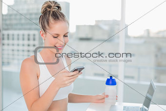 Laughing sporty blonde sending a text