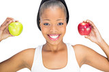 Fit smiling woman holding red and green apple while looking at camera